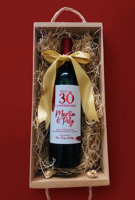 Botella de vino en caja de madera con virutas, moño dorado y etiqueta de aniversario 30 con nombres Martin y Pily y mensaje de bendición