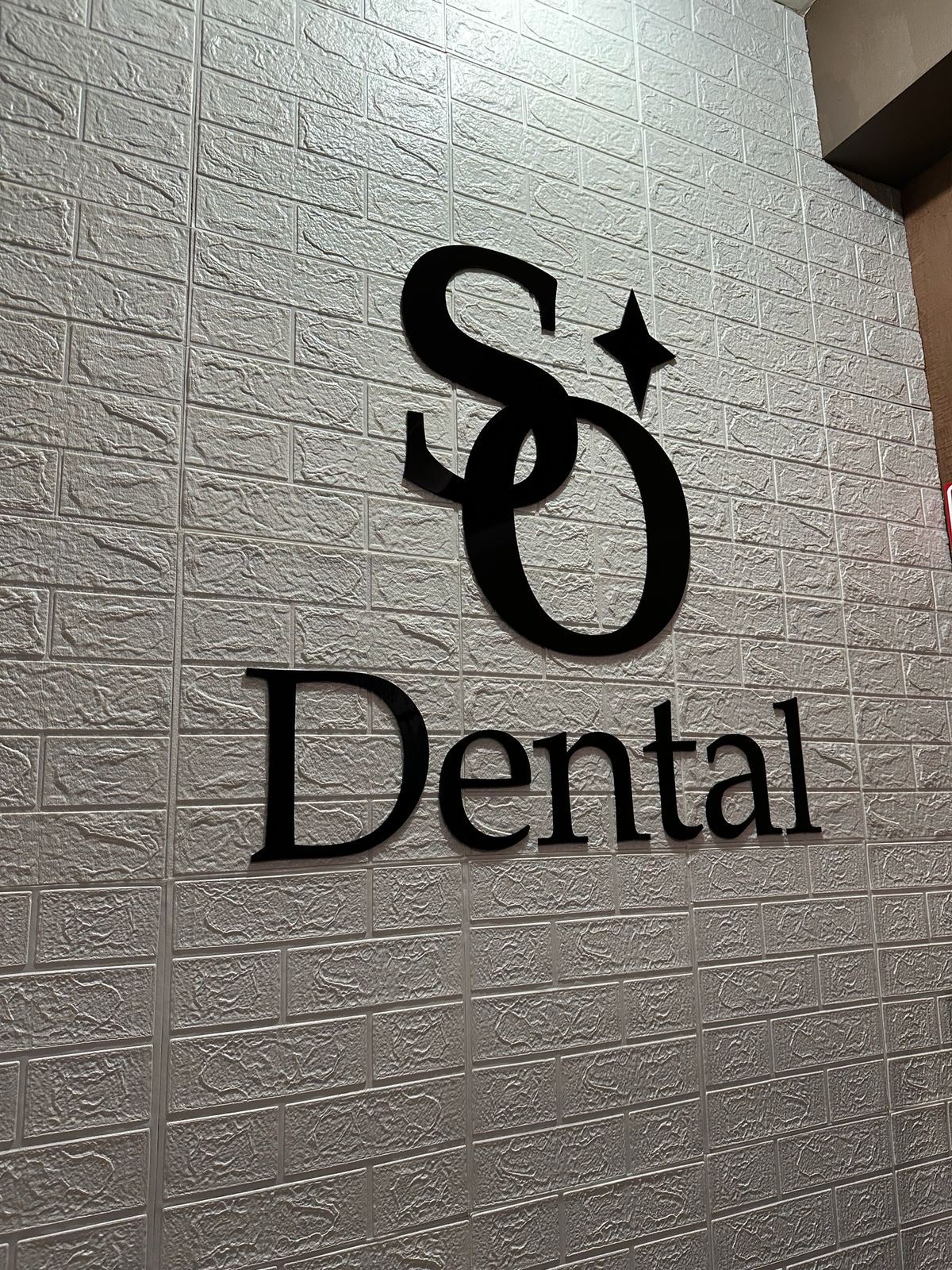 Letrero comercial de acrílico negro 3D para clínica SO Dental sobre pared de ladrillo blanco